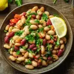 A serving of dense bean salad garnished with fresh herbs and a lemon wedge, ready to enjoy.