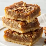 Enjoy Homemade Easy Pecan Pie Bars Today 11 Stack of gooey pecan pie bars with a golden crust and nut topping.